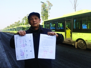 劉明手持多個(gè)部門的審批文件，身后就是閑置在路邊的電動(dòng)公交車